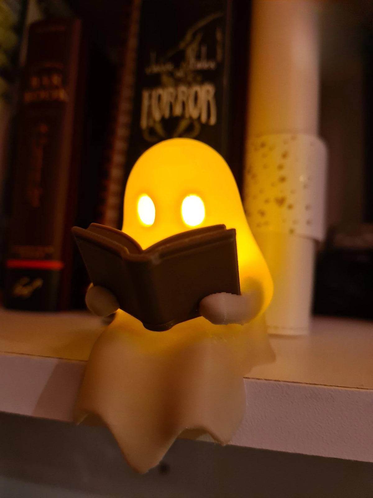 Cute Little Ghost Sitting on A Shelf Reading A Book with Flickering Ornament