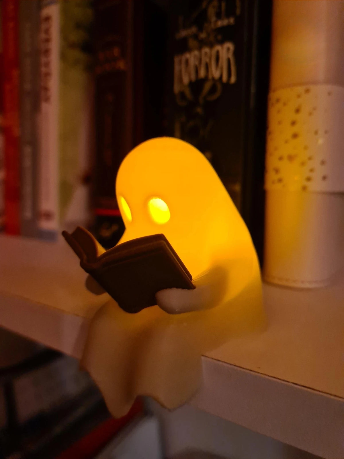 Cute Little Ghost Sitting on A Shelf Reading A Book with Flickering Ornament